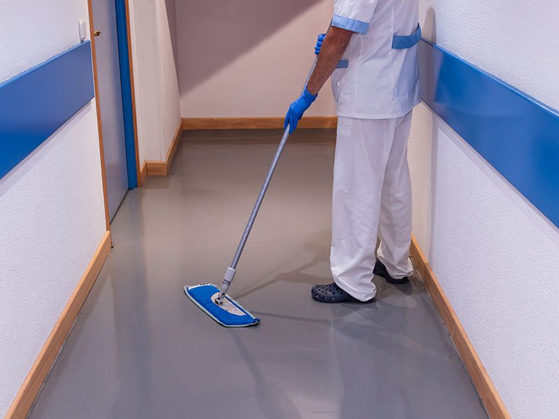 Custodial worker cleaning floor using mop in corridor.
