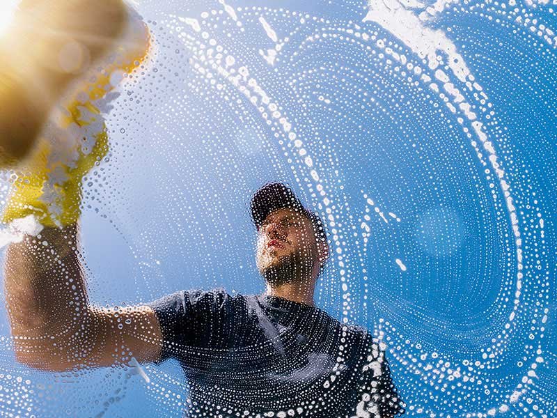 Cleaner washing glass surface from outside with soapy water.